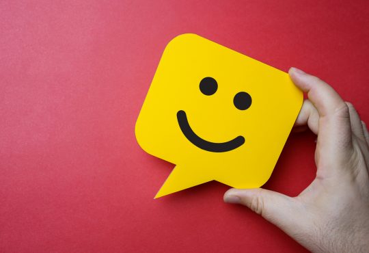 Man holding yellow speech bubble with smiley face on red background.