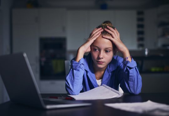 Schoolgirl learning via internet with laptop at home.