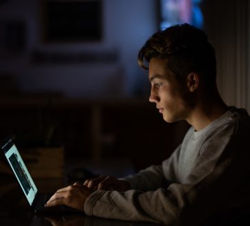 close up of one caucasian teenager working or studying alone at home at night with his laptop
