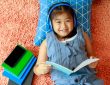 little girl lying on floor of bedroom reading and listening through headphones