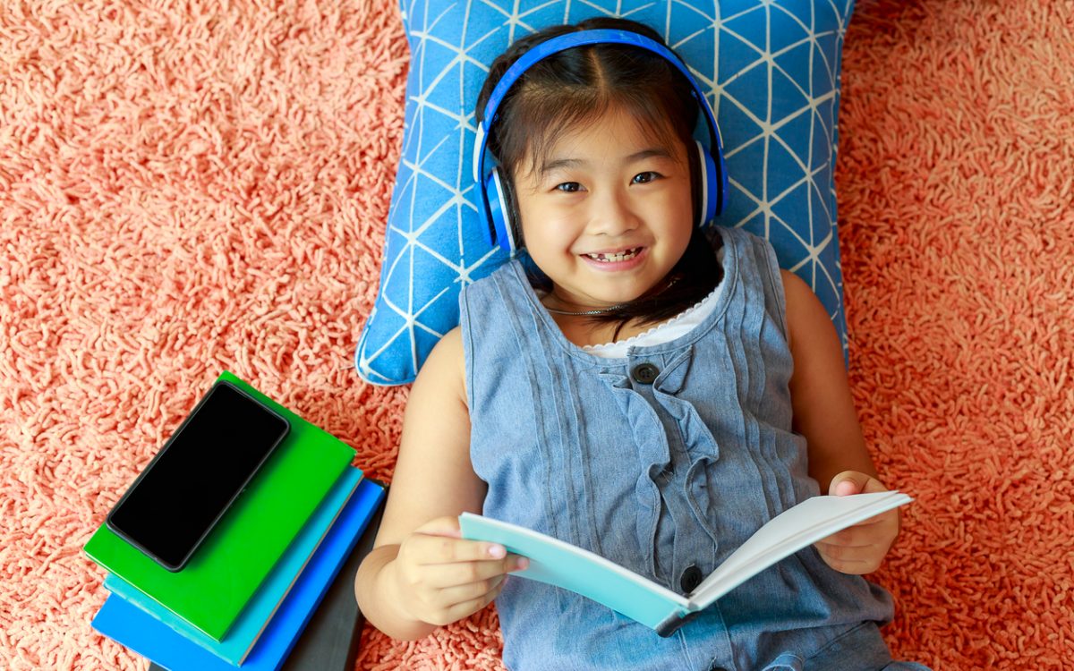 little girl lying on floor of bedroom reading and listening through headphones