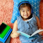 little girl lying on floor of bedroom reading and listening through headphones