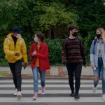 Four college students walking across crosswalk wearing masks.