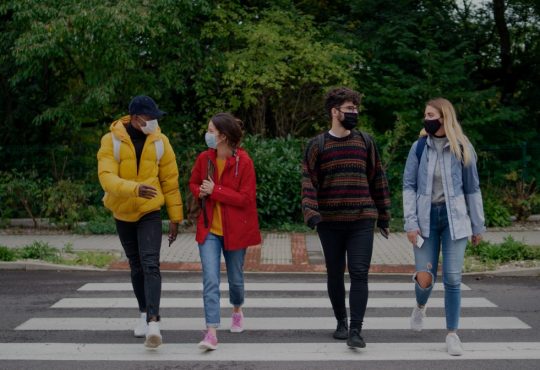 Four college students walking across crosswalk wearing masks.