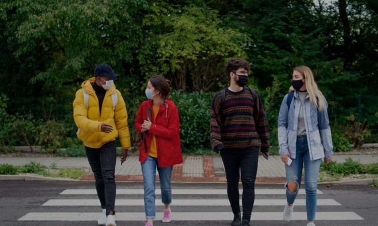 Four college students walking across crosswalk wearing masks.