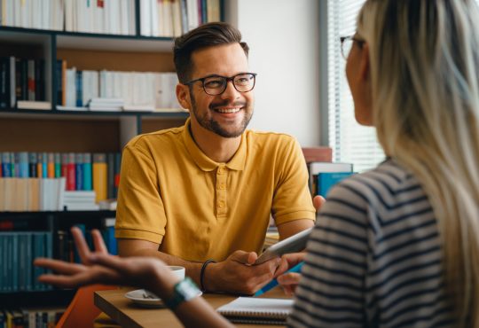 Female student talking to male university advisor in office.