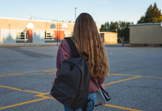 Teen girl walking through school's outdoor basketball court.