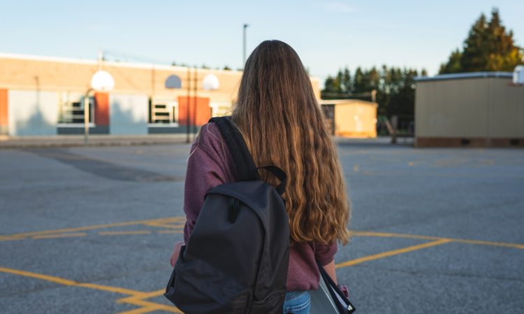 Teen girl walking through school's outdoor basketball court.
