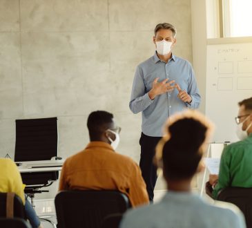 University professor wearing protective face mask while holding a class to group of students during coronavirus epidemic.