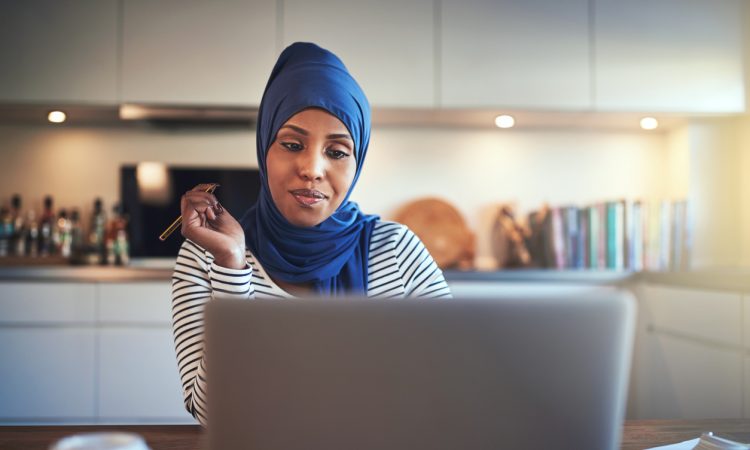 Woman wearing hijab working at kitchen table.