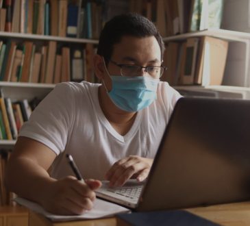 Man using laptop in library wearing mask.