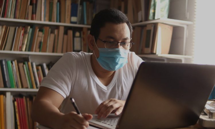 Man using laptop in library wearing mask.