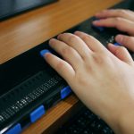 Close-up of hands using computer with braille display.