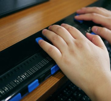 Close-up of hands using computer with braille display.