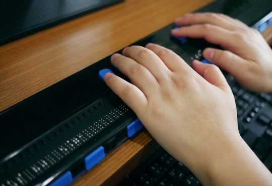 Close-up of hands using computer with braille display.