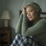 Middle-aged woman sitting in bed wearing pyjamas and looking worried