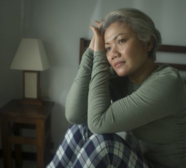 Middle-aged woman sitting in bed wearing pyjamas and looking worried