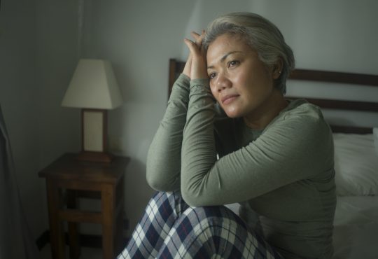 Middle-aged woman sitting in bed wearing pyjamas and looking worried