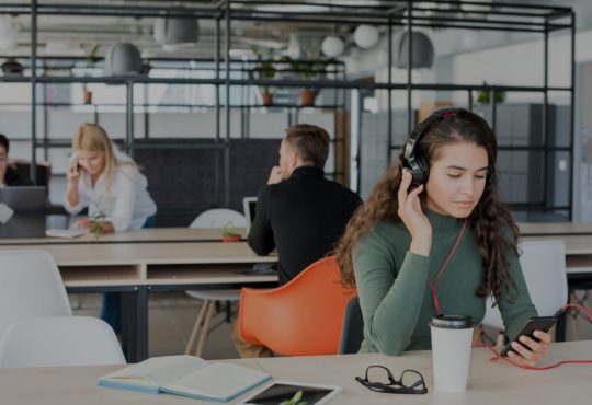 Young woman wearing headphones in open-concept office.