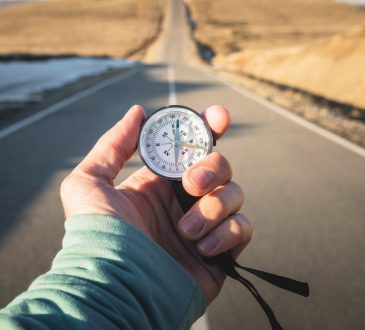 Compass in hand in front of mountain road background.