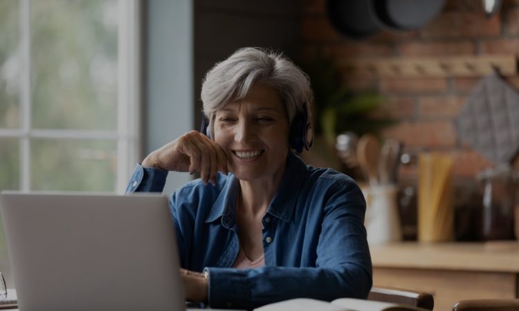 Older woman watching something on laptop screen at home.