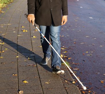 A blind person walking on the street using a red and white walking stick.