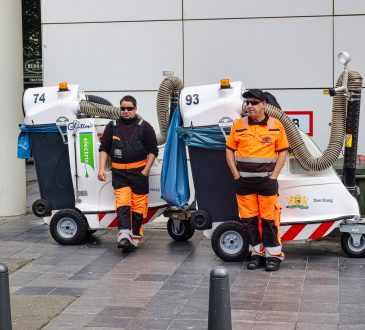 Workers standing beside street cleaning machines.