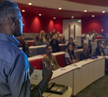 Man lecturing students in a university lecture theatre.