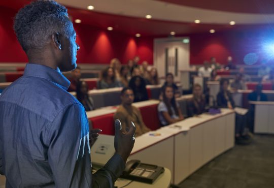 Man lecturing students in a university lecture theatre.