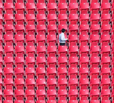 One person walking among empty red stadium seats.