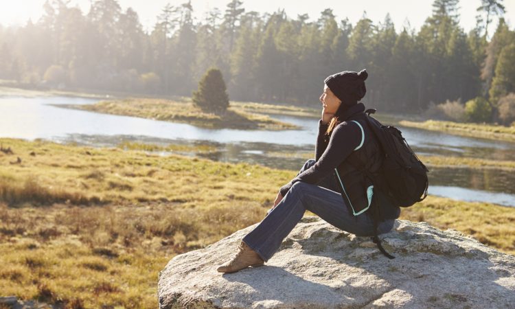 Young woman sits on a rock in countryside admiring the view