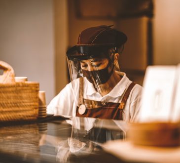 Woman wearing face shield working behind cafe counter.