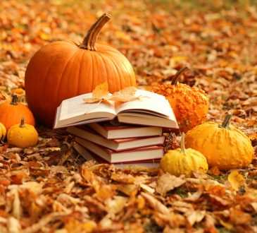 Stack of books and orange pumpkins set on autumn foliage