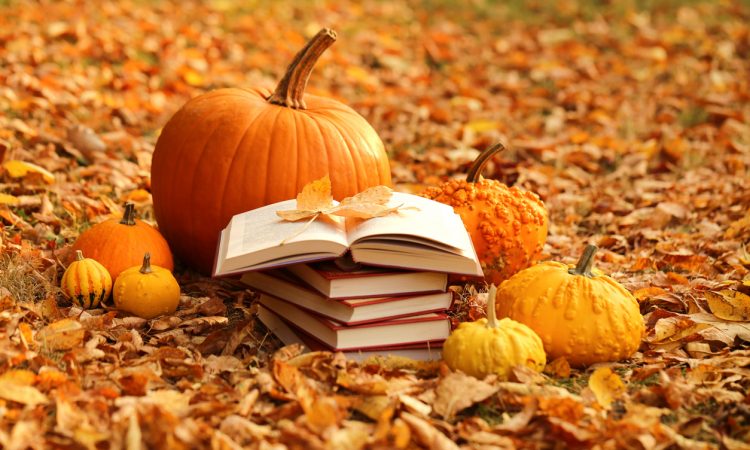 Stack of books and orange pumpkins set on autumn foliage
