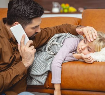 Father checking temperature of sick daughter lying on couch