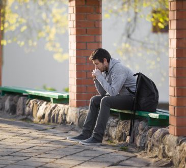 Stressed male student sitting on bench outside.
