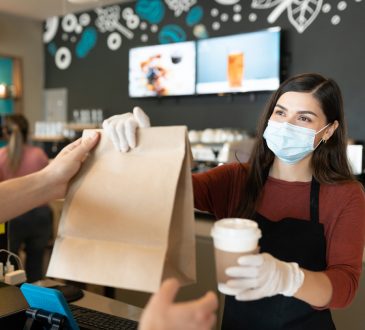 Young female staff giving parcel and coffee to customer at takeaway counter in coffee shop