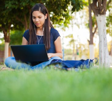 Teenage girl using a laptop and earbuds outdoors