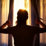 Silhouette of a young woman at the window opening curtains.