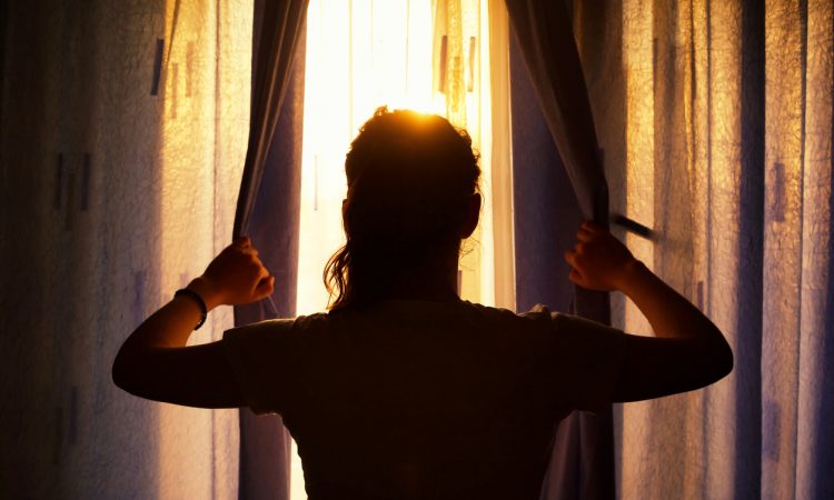 Silhouette of a young woman at the window opening curtains.