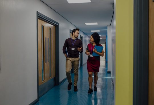 Man and woman walking down school hallway talking.
