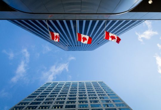 Canadian flags on skyscraper buildings seen from underneath
