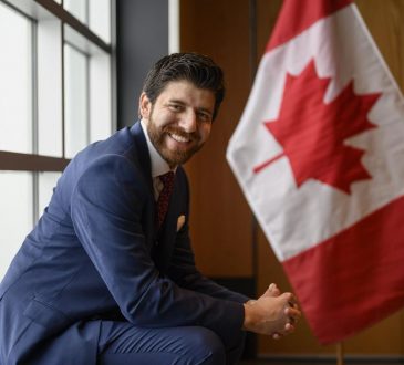 Tareq Hadhad sits beside a Canadian flag.