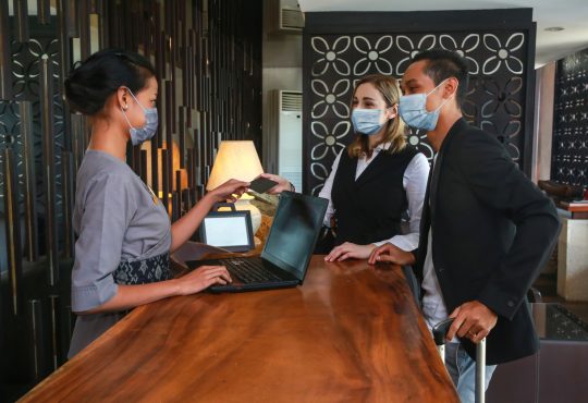 Couple and receptionist at counter in hotel wearing medical masks
