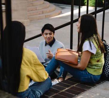 Three students sitting and talking on stairs outside.