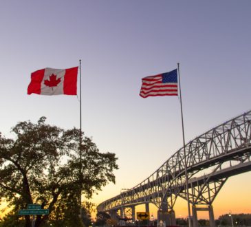 Canadian and American flags in front of Blue Water Bridges crossing.