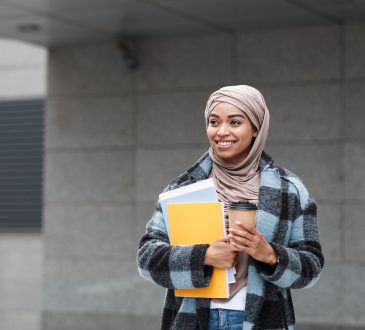 Student holding books and coffee cup