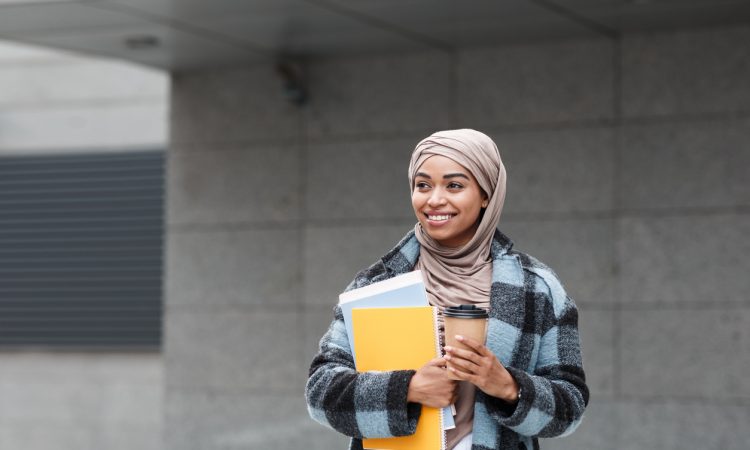 Student holding books and coffee cup
