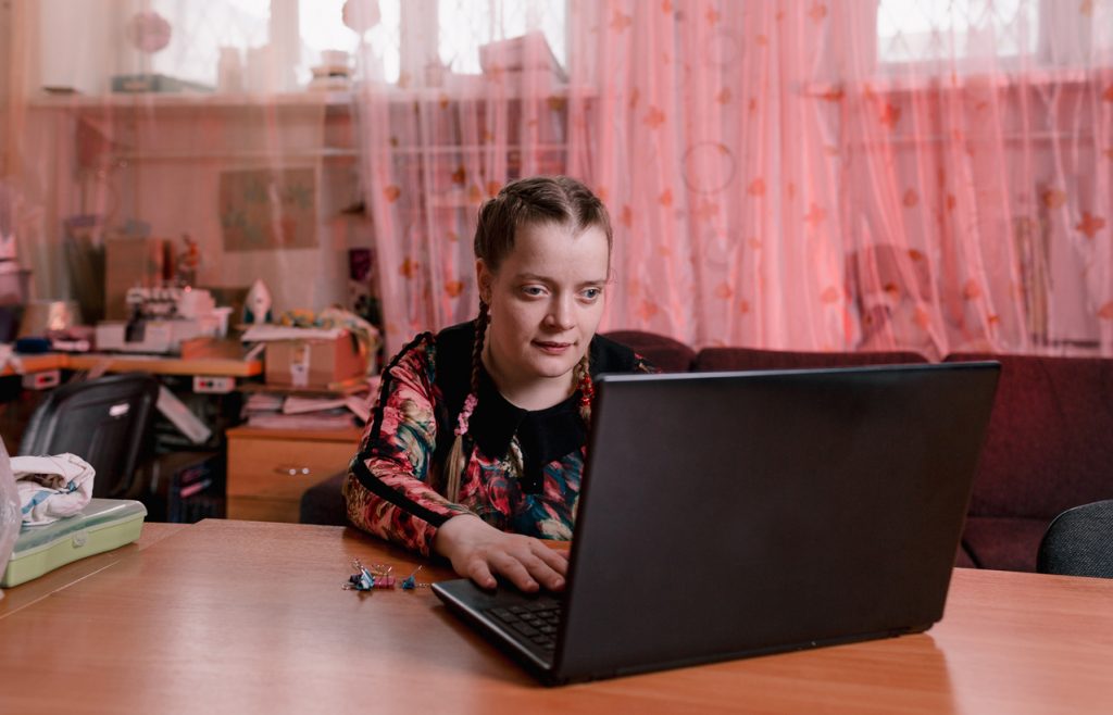 Young woman typing on laptop in bedroom.