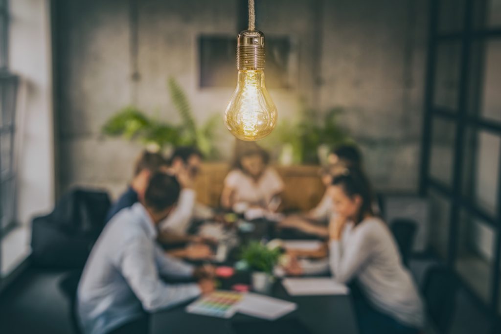 Lightbulb hanging in front of people working together around table
